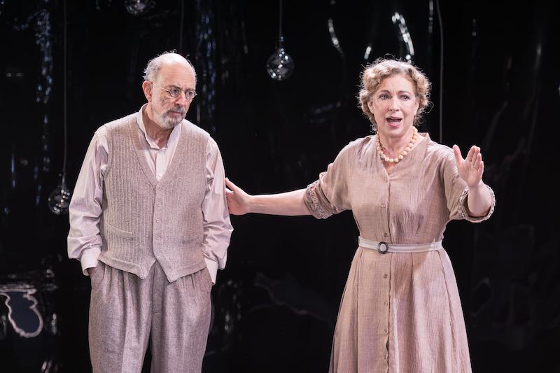 Richard Schiff stands and listens, while Alex Kingston is speaking