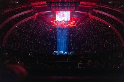 a wide angle picture of the Albert Hall, the crowd in darkness, the stage dramatically lit in red